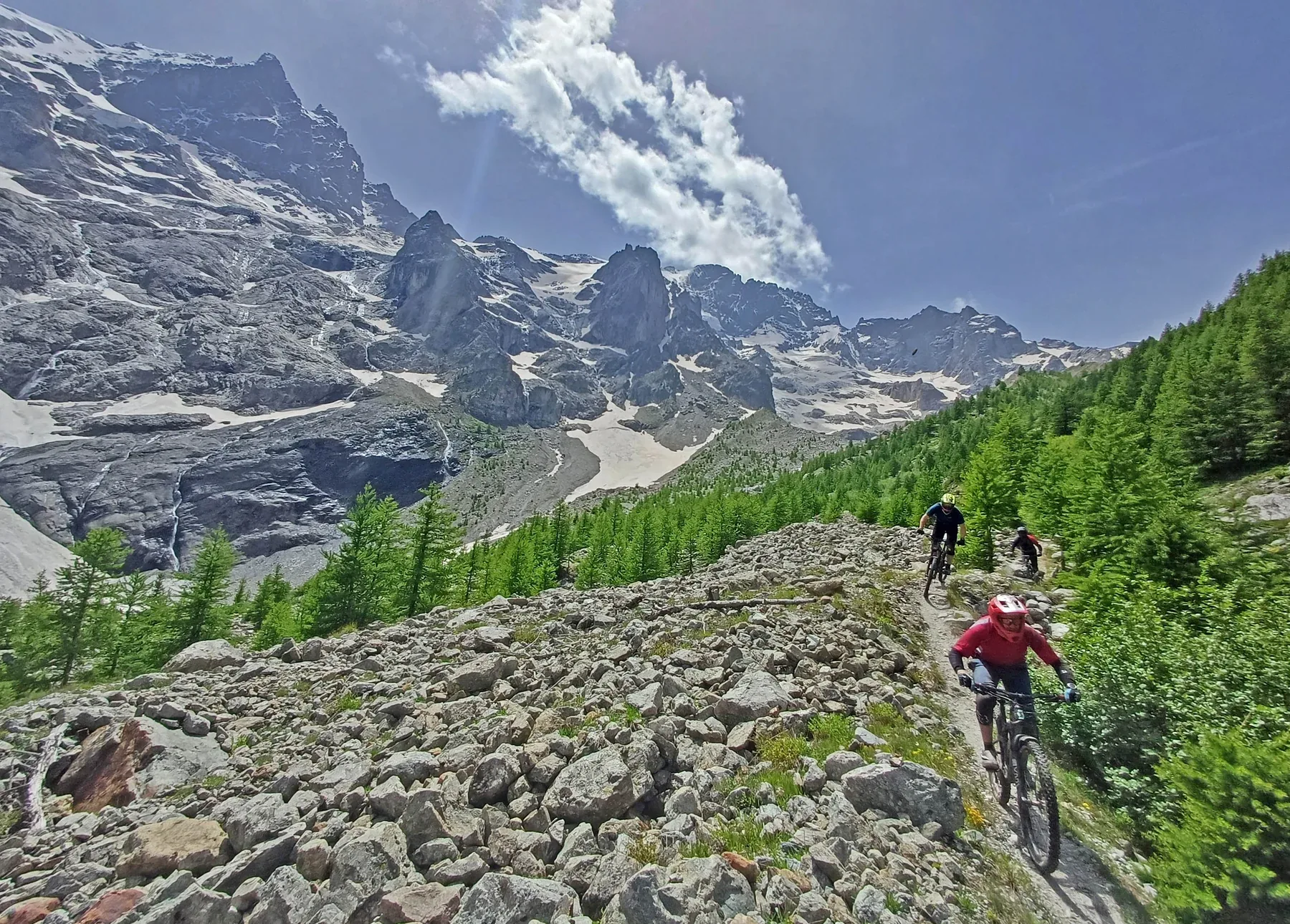 Mountain bikers descending a rocky trail beneath glaciers and Alpine peaks