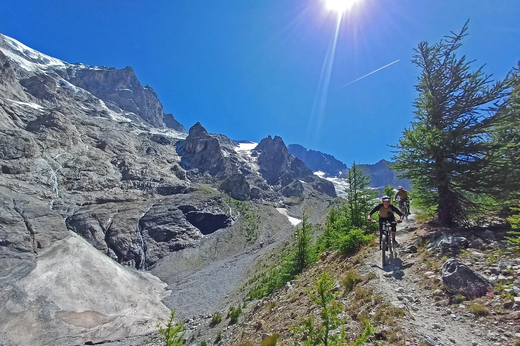 Mountain bikers descending a rocky trail beneath snowy Alpine peaks