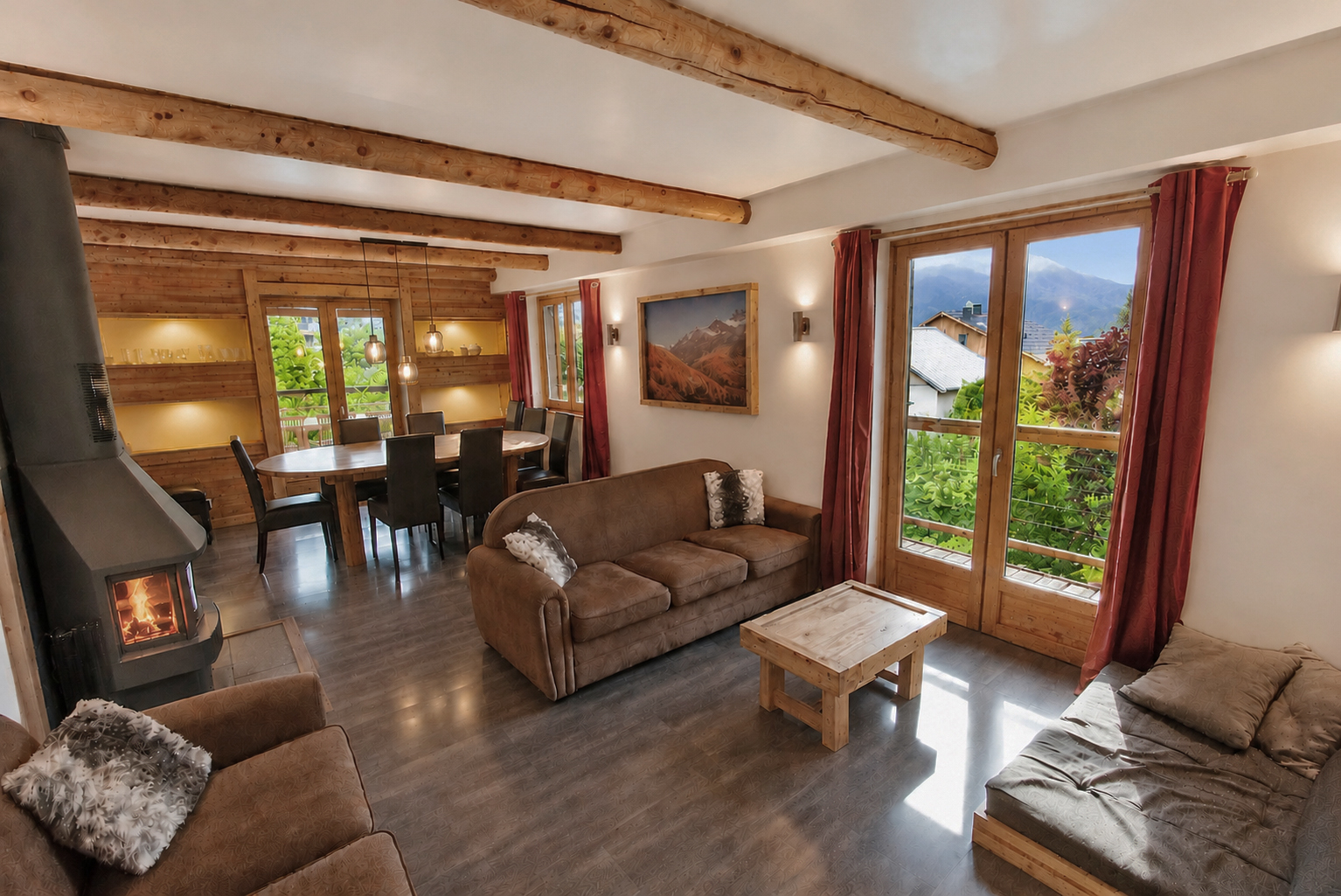 Chalet living and dining room with timber beams, a wood stove, sofas and mountain views