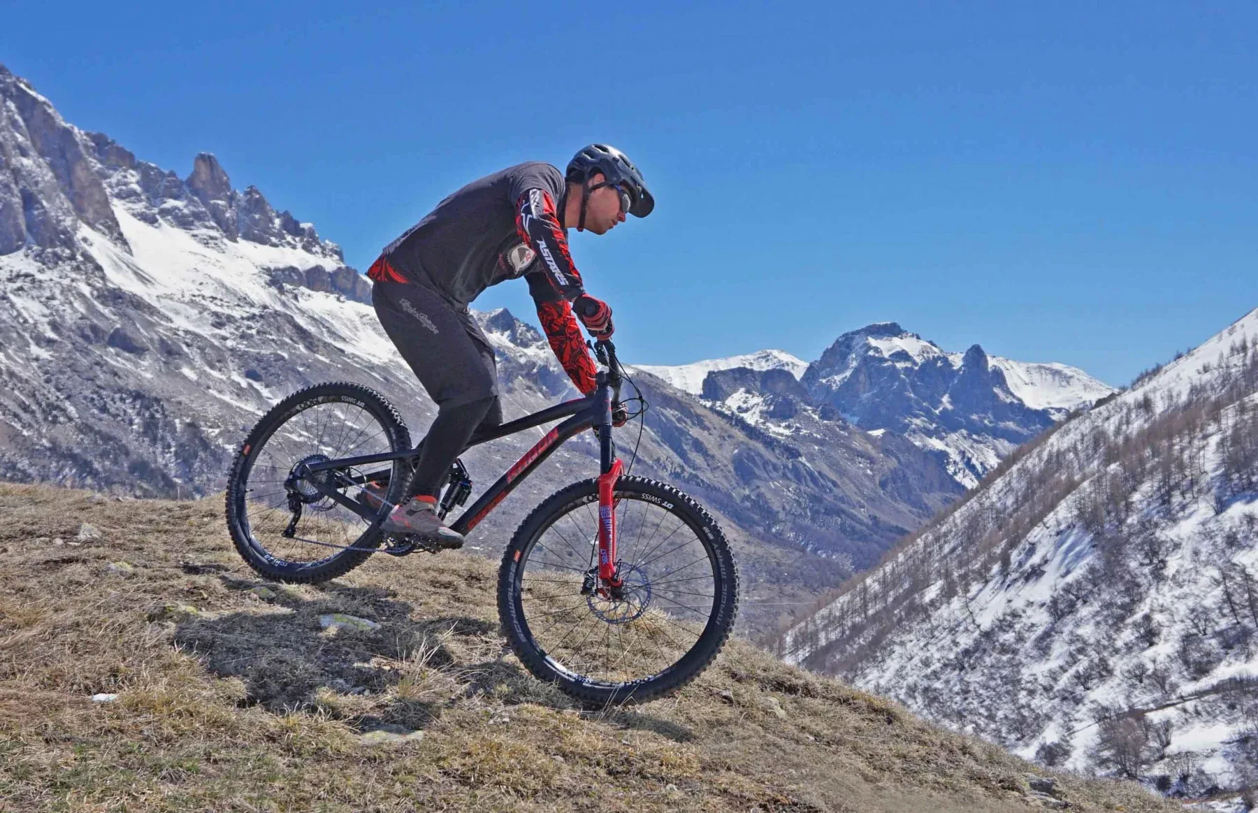 Mountain biker riding a rocky Alpine trail beneath snow-covered peaks