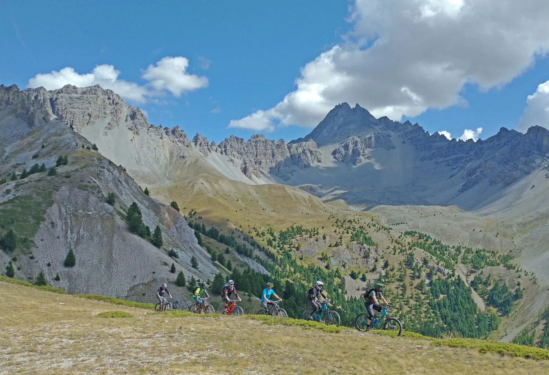 Group of mountain bikers traversing an Alpine meadow beneath rugged peaks