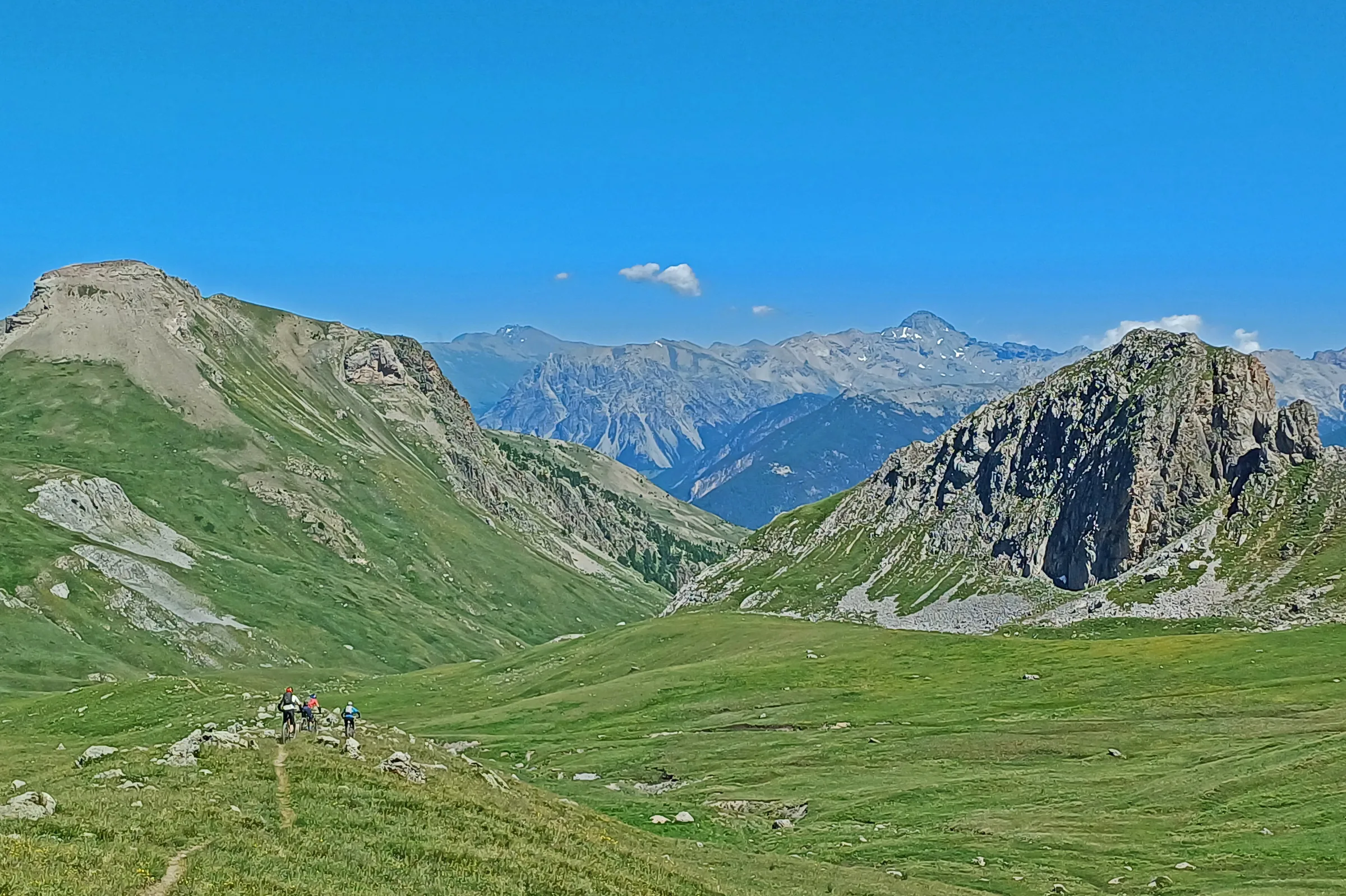 Small group of mountain bikers crossing a broad green Alpine meadow