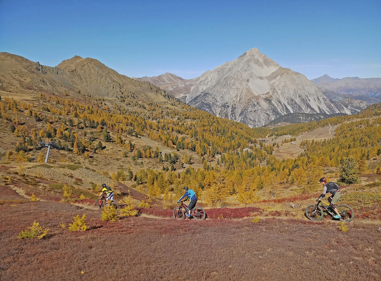 Mountain bikers crossing an autumn meadow beneath an Alpine peak