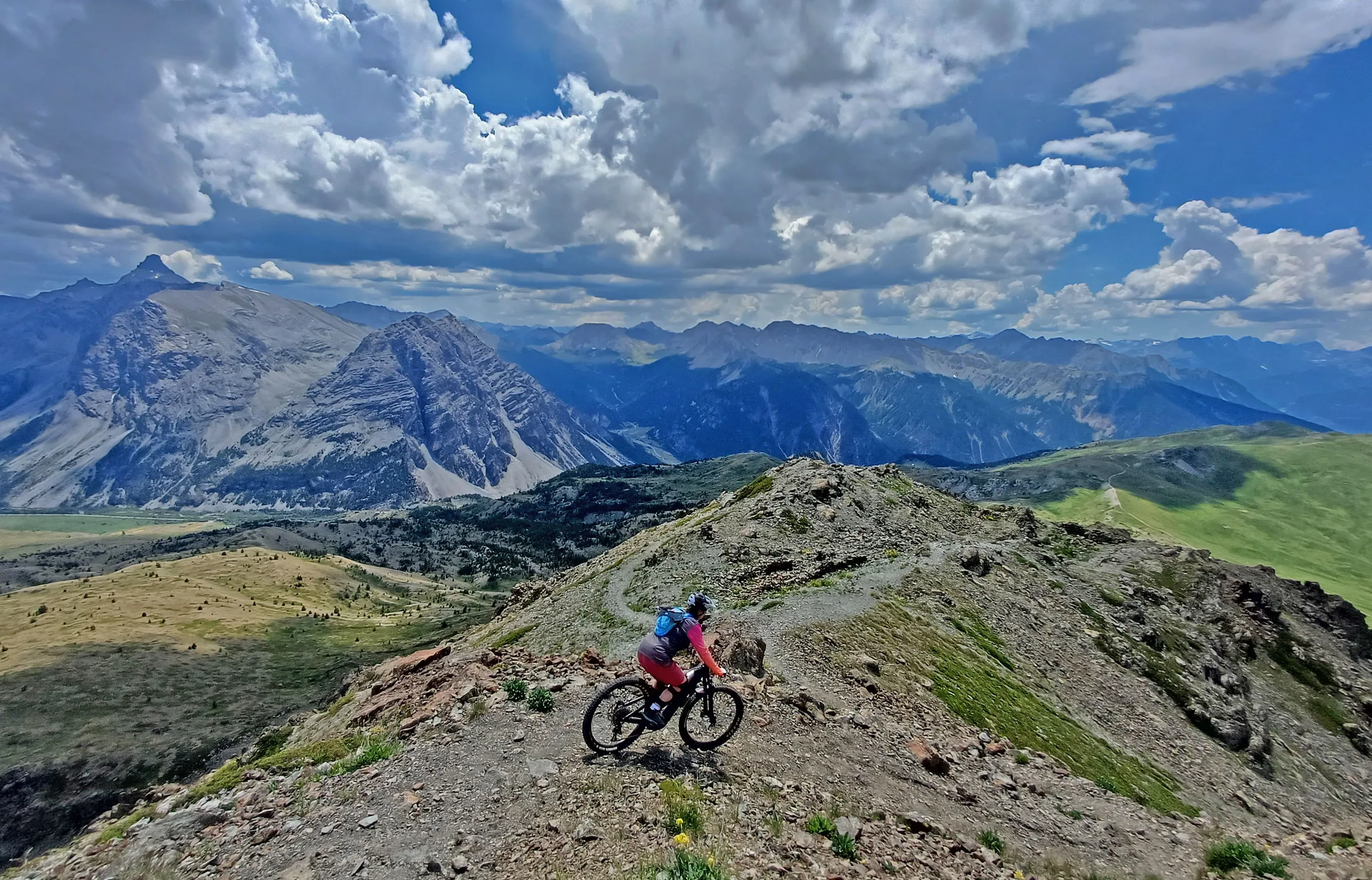 Mountain biker riding across an open grassy ridge beneath dramatic clouds
