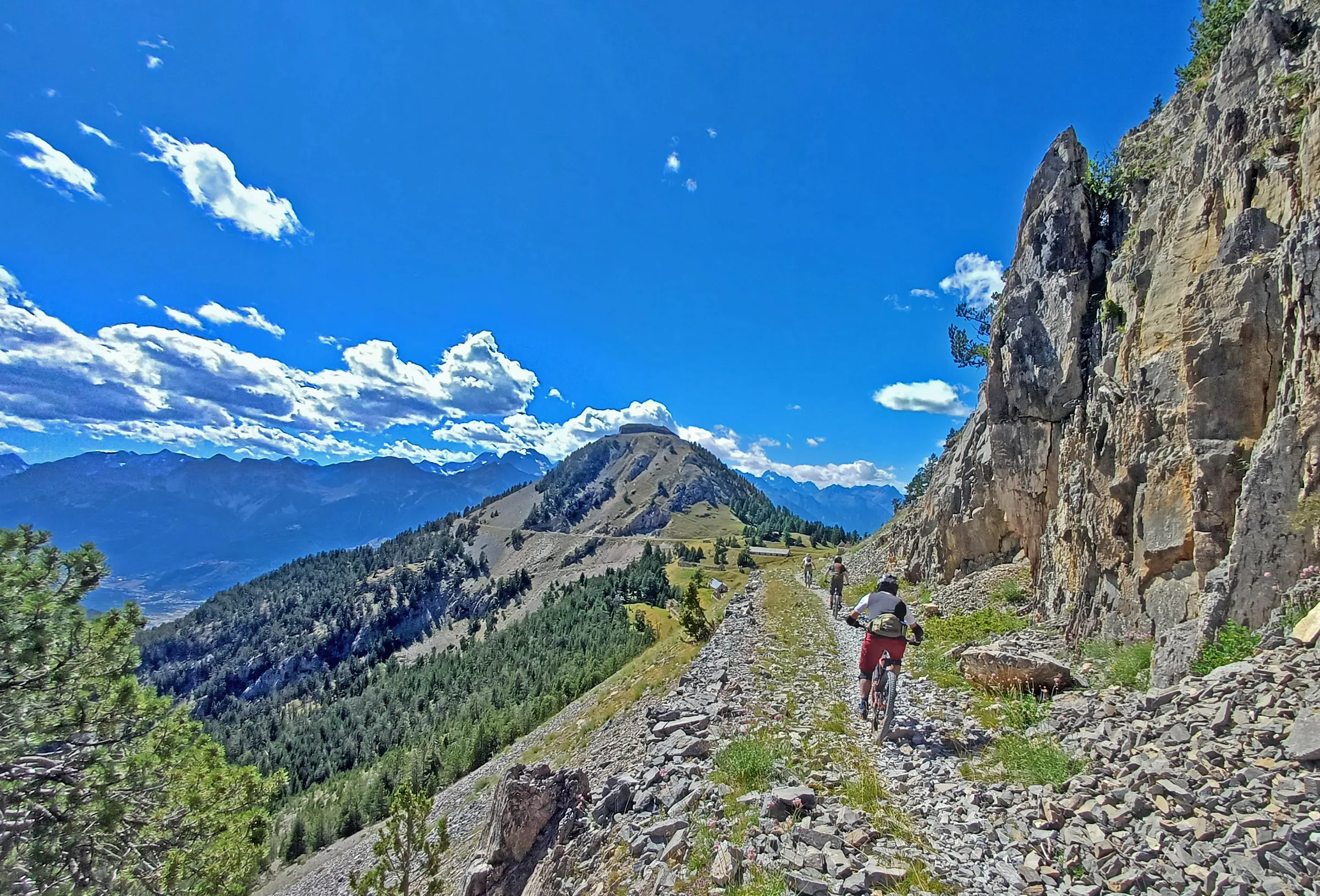 Mountain biker descending a rugged trail beneath a steep rocky cliff