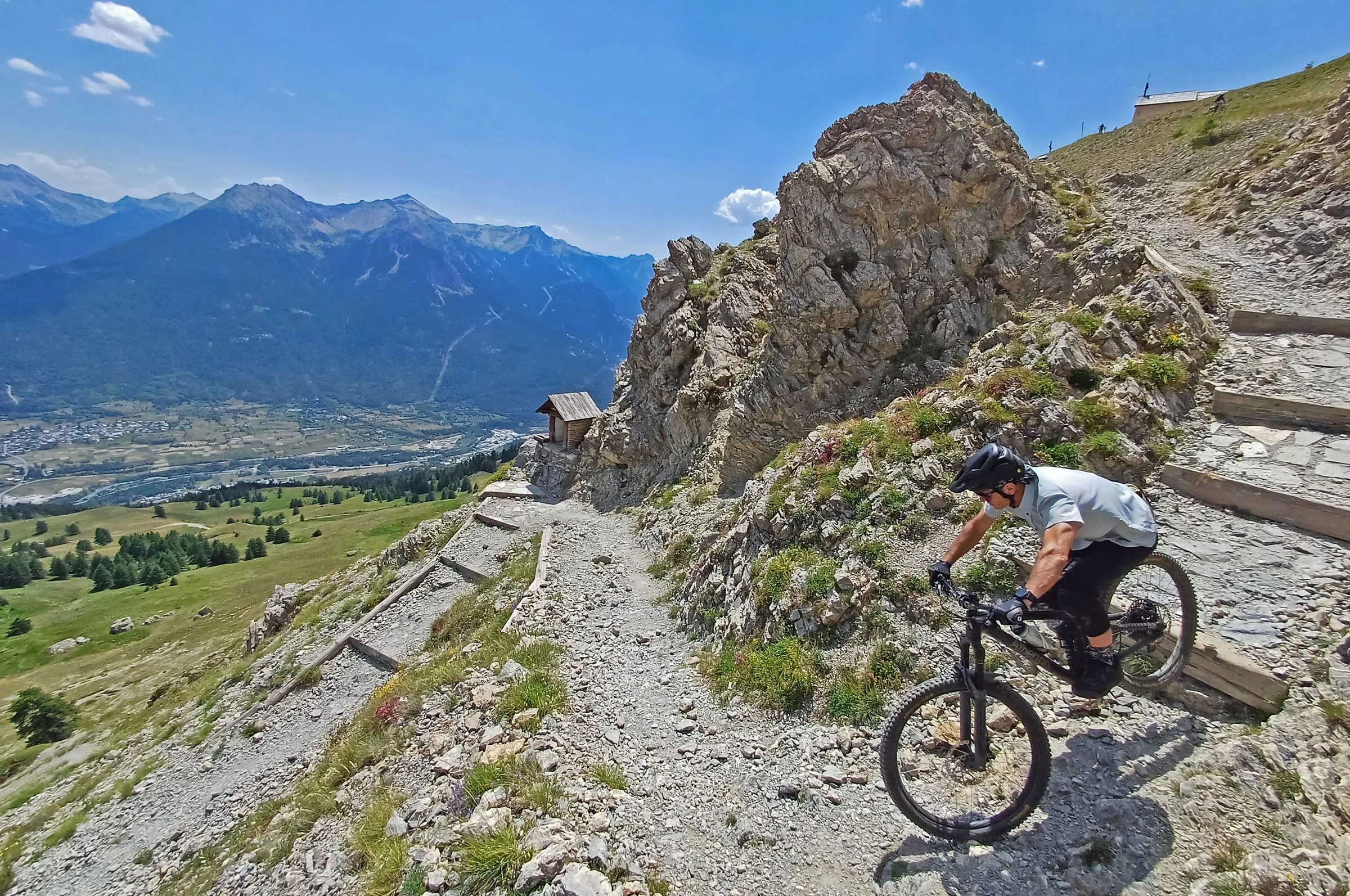Mountain biker descending a rocky high-Alpine trail above a wide valley