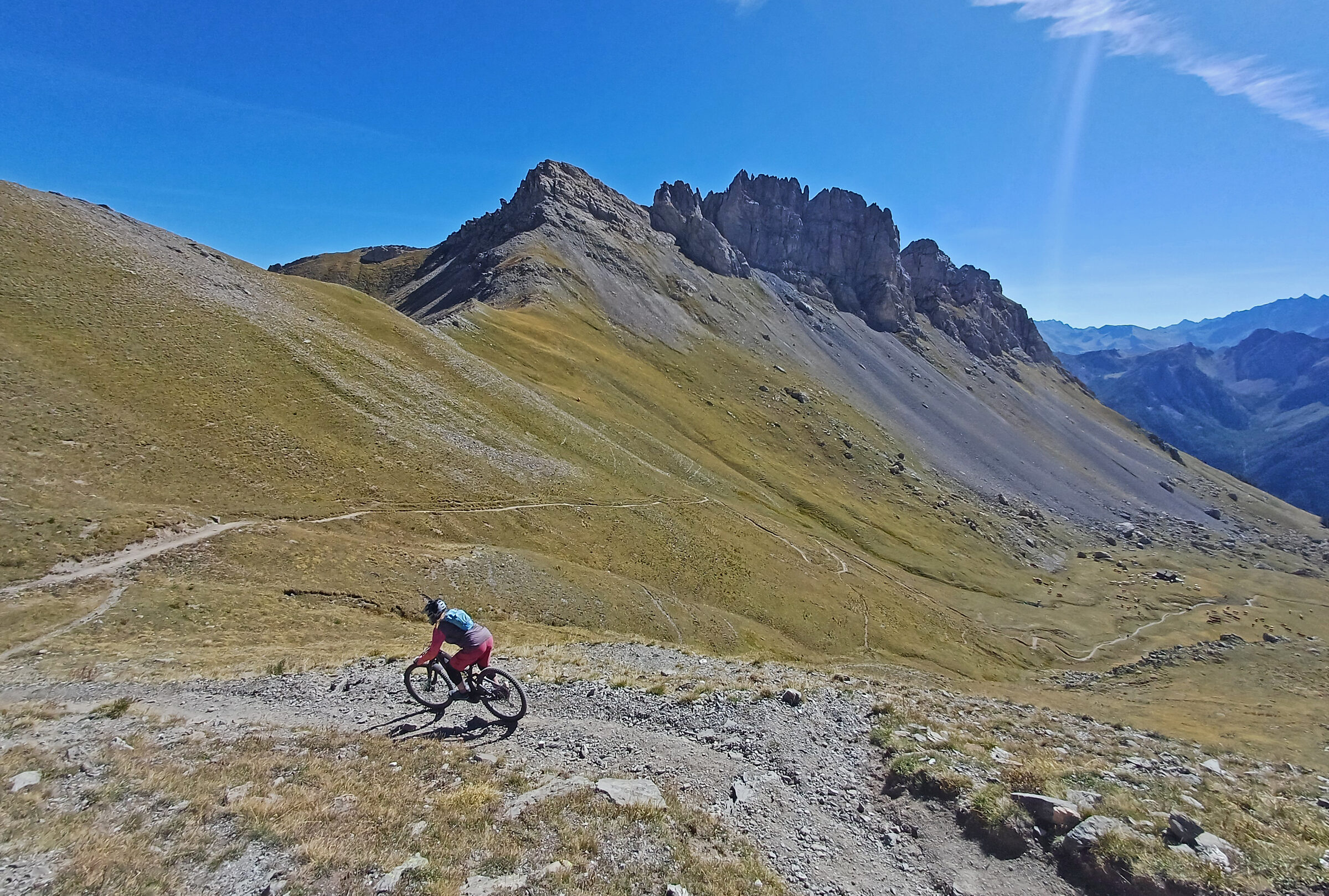 A mountain biker descending a high Alpine trail beneath a rugged mountain ridge